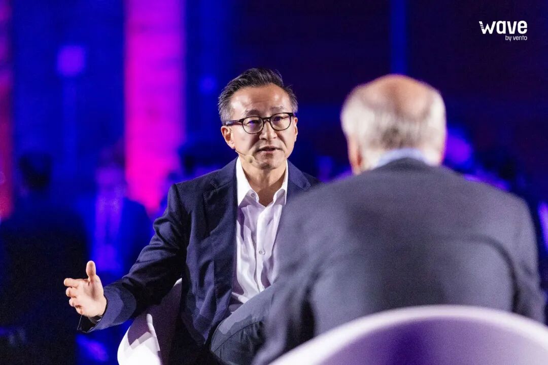 Joe Tsai of Alibaba speaking at a tech summit, with a presentation slide showing a three-layer AI architecture